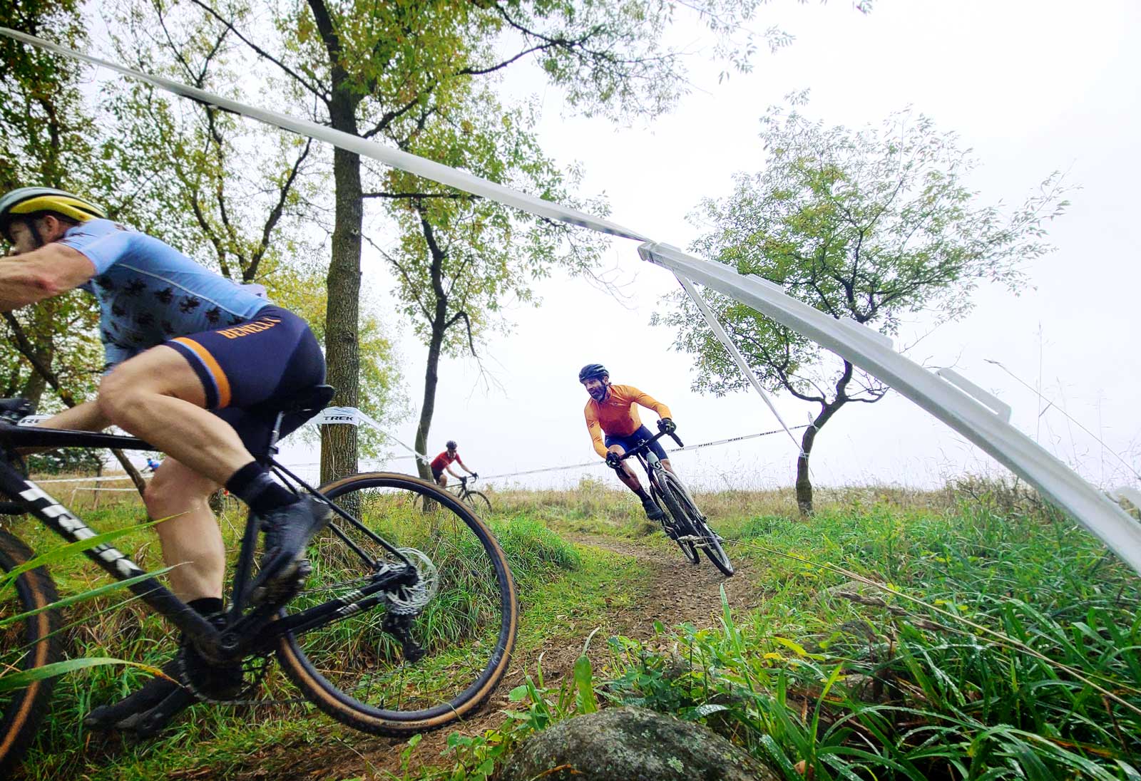 Three cyclocross racers wend their way through damp farmland.